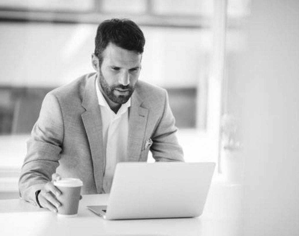 Geschäftsmann sitzt mit Coffe-to-go am Laptop